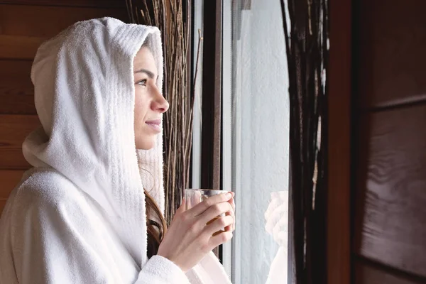 Красива Жінка Білому Халаті Біля Вікна Тримає Чашку Гарячим Напоєм — стокове фото