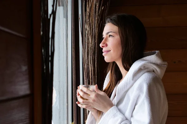 Красива Жінка Білому Халаті Біля Вікна Тримає Чашку Гарячим Напоєм — стокове фото