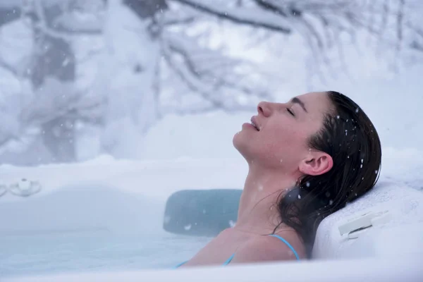 A beautiful woman in the whirlpool relaxes, breathes clean air, and is happy  in the middle of nature as the snow falls from the sky. Concept of: relaxation, nature, wellness.