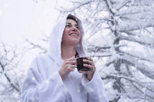 白いバスローブで美しい女性は 雪が空から落ちている間山で熱いお茶を飲みます リラクゼーション — ストック写真