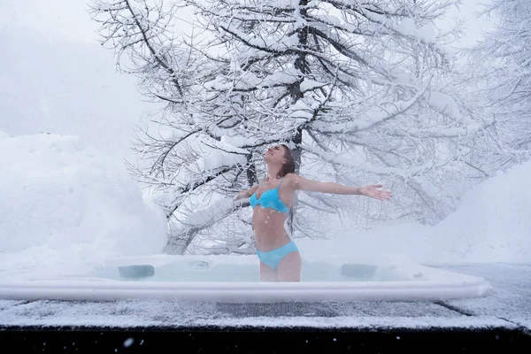 A beautiful woman in the whirlpool relaxes, breathes clean air, and is happy  in the middle of nature as the snow falls from the sky. Concept of: relaxation, nature, wellness.
