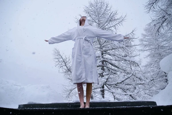 A beautiful woman in the whirlpool relaxes, breathes clean air, and is happy  in the middle of nature as the snow falls from the sky. Concept of: relaxation, nature, wellness.