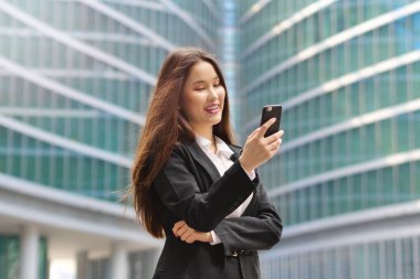 Bir takım elbise ve kravat, mutlu ve telefon, ofis dışında kullanarak iletileri ve denetimleri e-posta yollama gülümseyen bir oryantal iş kadın portresi. Kavramı: teknoloji, ağ, başarı.