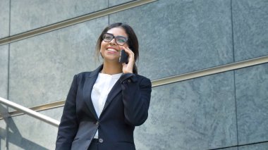 Gülümseyen, mutlu, genç güzel iş kadını (öğrenci) bir takım, merdivenlerden adımları, telefon, konuşan bir mesaj yazma. Konsept: yeni iş, iletişim, Arap, bankacı, Gözlük, çağrı