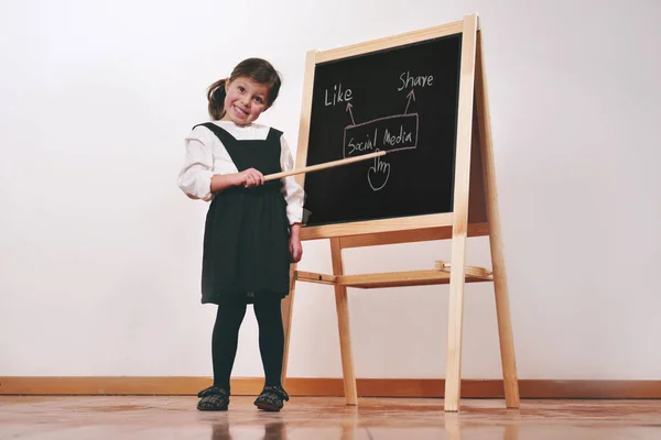 A happy little girl dressed as a teacher in front of a small blackboard holds a lesson in economics, marketing, teamwork, mathematics. Concept of: educational, school, business and love for study.