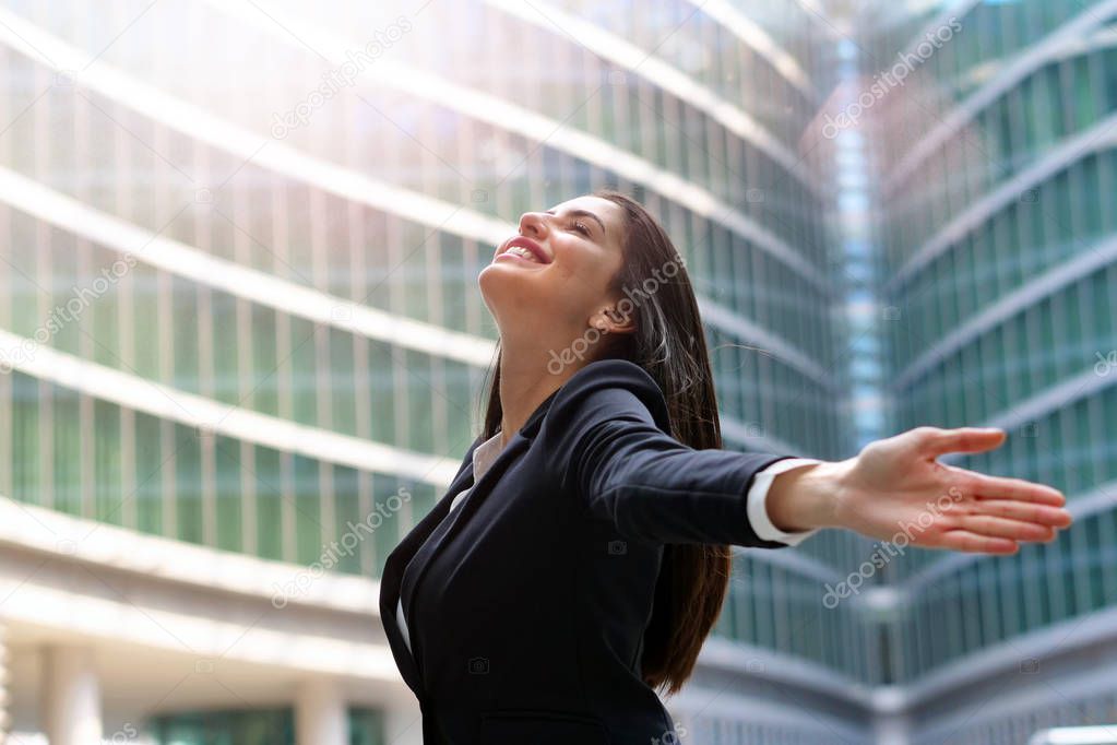 A business woman, dressed in a suit, raises her arms to the sky and breathes as a sign of freedom and success in her work.