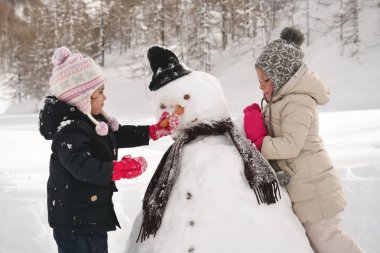 Karla, dağlarda bir kış gününde iki küçük kız oynamak ve kardan adam oynamak. Kavramı: kış tatilleri, oyunu, Noel, dağ