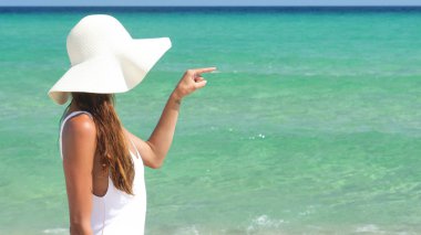 Yanık tenli bir kadın için deniz, mavi deniz suyu olan bir arka planda beyaz şapkalı, beyaz bir mayo içinde denize bakarak ile onu geri duruyor.