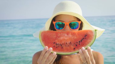 Kız bir karpuz deniz kenarı deniz arka plan düzenliyor. Konsept: deniz dinlenme, gıda, Güneş, seyahat, taze meyve, tatil, kırmızı sulu karpuz, berry, siyah tohumlar, diyet, yaz.