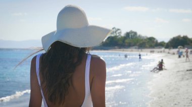 Güzel genç kadın, mutlu hissediyor musun, arka kapağı transparan, beyaz mayo, beyaz hasır şapka, beyaz şal, ile mavi su, kum deniz arka plan ayakta. Konsept: güneş, seyahat, tatil, özgürlük, diyet, dinlenme, deniz.
