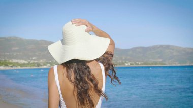 Güzel genç kadın, mutlu hissediyor musun, arka kapağı transparan, beyaz mayo, beyaz hasır şapka, beyaz şal, ile mavi su, kum deniz arka plan ayakta. Konsept: güneş, seyahat, tatil, özgürlük, diyet, dinlenme, deniz.