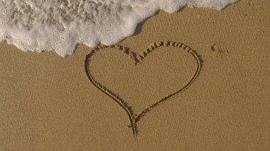 Güzel kahverengi kumlu plaj ve okyanus dalgaları üzerinde kalp boyalı 