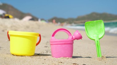 Çocuk formları sarı kova, yeşil kürek ve pembe sulama olabilir, farklı renkler, arka plan, kum ve deniz.