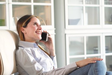 Bir kadın onun oturma odasında onun şezlong veya kanepe rahatlatır, pencereden görünüyor, telefon kullanır ve rahatlık ve dinlenme sahiptir. Kavramı: Ev, rahatlama ve konfor.