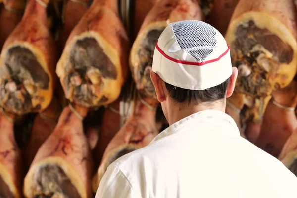 In a ham factory, a man in charge of quality control walks between the hams and controls, the perfume and the certified Italian quality. Concept of: tradition, Italy, food, ham