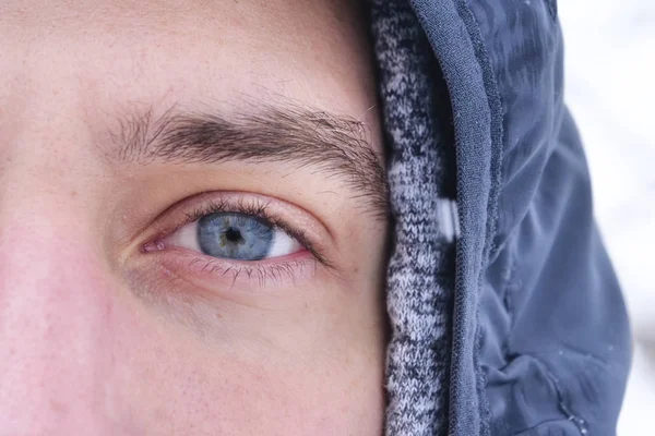 Close up of a blue eye of a man watching in the room while the snow falls from the sky in slow motion. Concept of: nature, eyes, magic moment, winter holidays