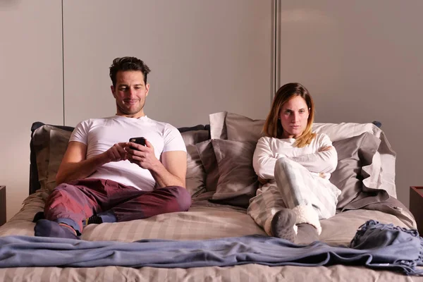 A married couple in bed use the phone separately to send messages or use social networks and no longer talk to each other. Concept of: new generations, separation, technology.