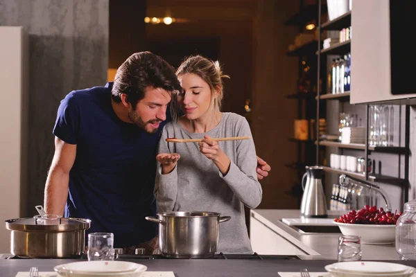 An engaged couple cook together and have fun while tasting the sauce they have prepared. The married couple embraces to show their love. Concept of: cooking, love, lifestyle.