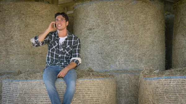 ハンサムな若い農夫 はシャツ Selfie メッセージを書いて 電話で話して 干し草の山に座って幸せ笑顔します コンセプト コミュニケーション 生態学 干し草 — ストック写真