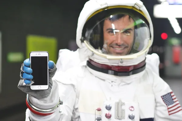 An astronaut dressed man uses the smartphone to call and send messages. The astronaut smiles while looking at the phone in his hand. Concept of: Phone Promotions, Messages and Spatial Calls.