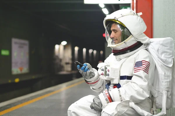 An astronaut dressed man uses the smartphone to call and send messages. The astronaut smiles while looking at the phone in his hand. Concept of: Phone Promotions, Messages and Spatial Calls.