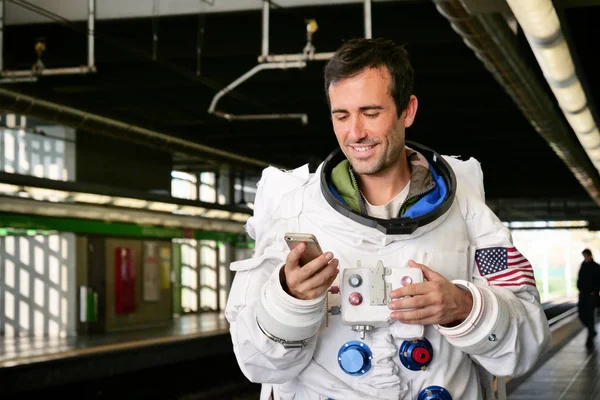 An astronaut dressed man uses the smartphone to call and send messages. The astronaut smiles while looking at the phone in his hand. Concept of: Phone Promotions, Messages and Spatial Calls.