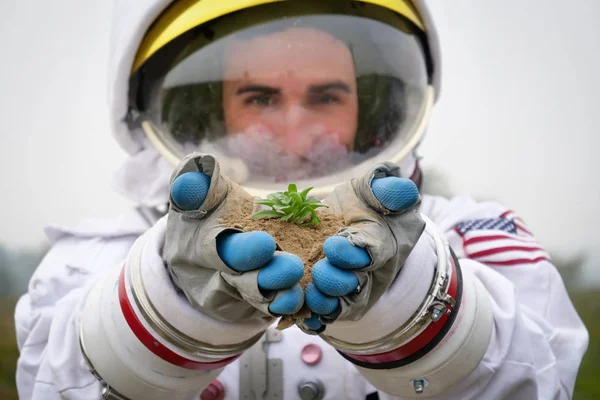 An astronaut lands on a planet all new and begins to examine new forms of plant life. He takes a sprout and hears it carefully. Concept of: ecological, new worlds and new life, exploration and science