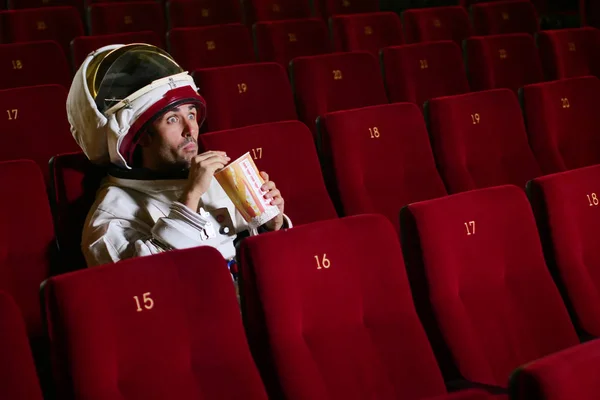 Astronaut looks at a movie while eating pop corn and enjoying the movie. Concept of: cinema and space films, film of the other world, surreal situations.