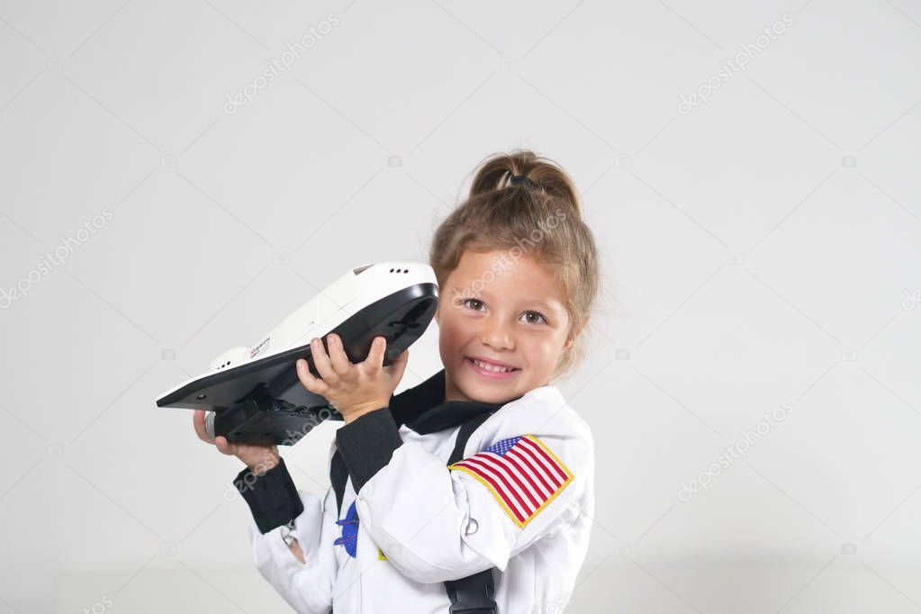 Portrait of a little girl dressed up by astronaut playing with shuttle and smiling while watching the camera. Concept of: ambition, success, children and their future.