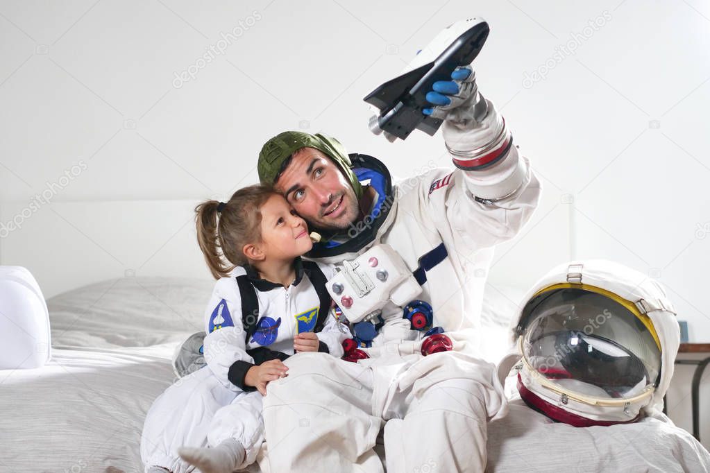 Romantic and family moments of dad and daughter playing with spacecraft, both dressed as astronauts and are happy at this unique moment. Concept of: love, family, home, games.