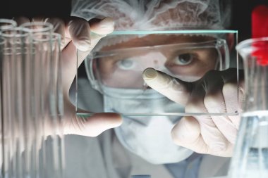 Fütüristik bir doktor, cerrah, teknolojik bir dijital holografik tabak, tıbbi maske, bir kap, kahverengi gözleri inceliyor. Konsept: futuristik tıp, yeni teknolojiler, doktorlar, laboratuvar, gelecek.