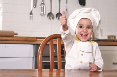 Mutfakta küçük bir kız portresi doğru beslenme ve gerçek gıda bir işareti olarak eliyle tamam yapma bir profesyonel aşçı gibi giyinmiş. Kavramı: beslenme, Aşçılık Okulu, eğitim.