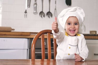 Mutfakta küçük bir kız portresi doğru beslenme ve gerçek gıda bir işareti olarak eliyle tamam yapma bir profesyonel aşçı gibi giyinmiş. Kavramı: beslenme, Aşçılık Okulu, eğitim.