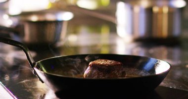 Orta yaşlı şef ile tahta kaşık restoran mutfakta tavada kızarmış et fileto salsa karıştırma (yakın)