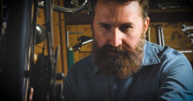 Anahtarı bir başarılı su kuyusu-damat yakışıklı sakallı ana hipster portresi, Bisikletler, onun atölye, tekerlekler, çerçeve, bir bisiklet tamiri uzman. Konsept: pro bisiklet, döngüsü tutku, yaşam biçimi.