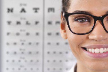 kısmi mutlu gülümseyen kadın gözlük gözlük takan ve Snellen görme keskinliği sınamak için kullanılan grafik ayakta optik Merkezi'ndeki görünümünü