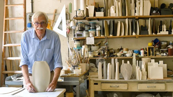 Portrait of an elderly artisan in his creative workshop who handmade clay and mold to create home-made jars and works of art. Concept of: handcraft, tradition, handmade artwork, creativity.