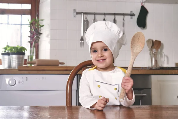 厨房里一个小女孩的肖像 她打扮成一个专业的厨师 面带微笑 手里拿着一个传统的木制厨房勺子 烹饪学校 教育和家庭 — 图库照片