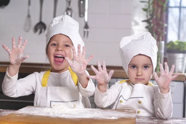 Two little girls in the kitchen prepare food, a dessert for the family. As they learn to cook they start playing with flour and smiling each other. Concept of: cooking classes, family, education.