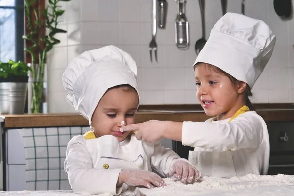 Two little girls in the kitchen prepare food, a dessert for the family. As they learn to cook they start playing with flour and smiling each other. Concept of: cooking classes, family, education.