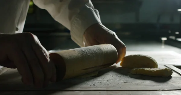 hands of a chef knead in Italian style in a professional kitchen with the rolling pin pizza dough and sweet Italian flavors and traditional Italian cuisine .