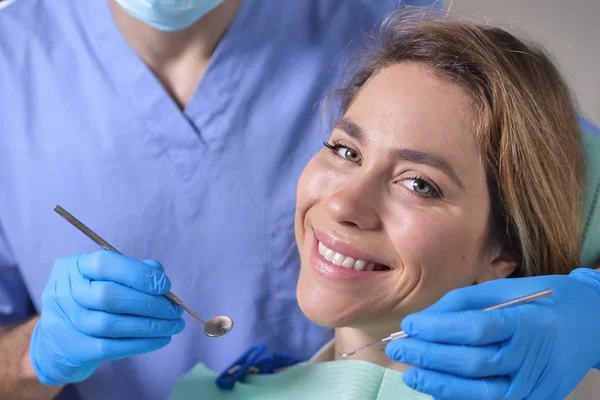 In a professional practice, a dentist checks the dentition of the patient, and she is happy with the visit, smiling, showing the perfect white teeth. Concept of: dentists, healthcare, perfect smile.