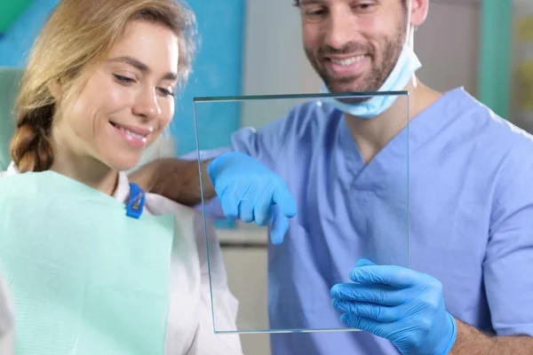 dentist doctor holding glass and showing to woman, checks patient denture plate