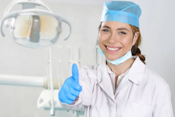 マスクの笑みを浮かべて 彼女の完璧な白い歯を見せて 手の親指を上げることで を作るとプロの歯科医師の女性のポートレート 歯科医療 完璧な — ストック写真