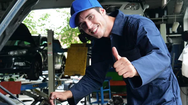 在一个车库里 一个机械师在检查和做完机器后 因为汽车已经成功修好了 他的拇指和微笑就可以了 — 图库照片