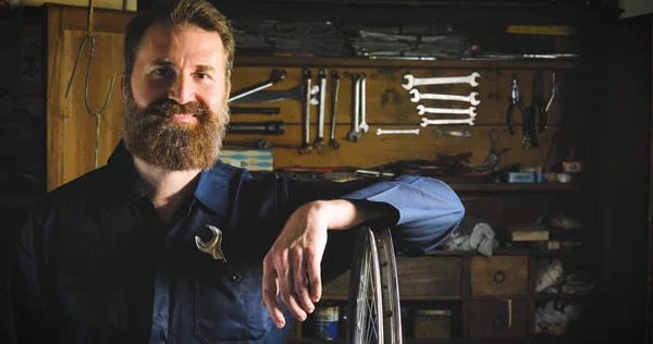 Portrait of a successful well-groomed handsome bearded master hipster, specialist in bicycles, repairing a bicycle in his workshop, wheels, frame, wrench. Concept: pro bike, cycle passion, lifestyle.