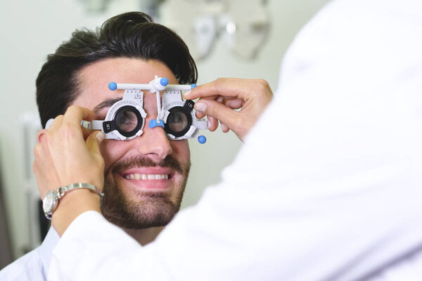 woman doctor checking man eyes with Calibrating eye test glasses phoropter
