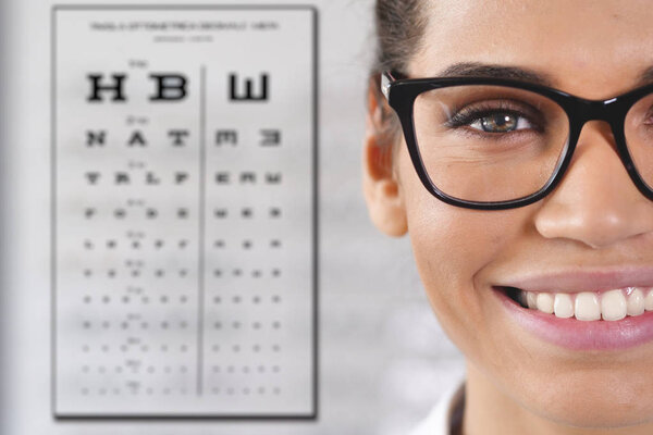 partial view of happy smiling woman in optical center wearing eyewear glasses and standing at Snellen chart used for visual acuity testing