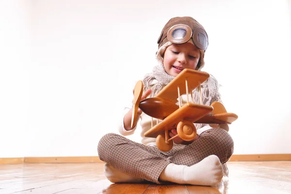 开玩笑可爱的小女孩打扮成飞行员坐在木地板上玩飞机玩具 — 图库照片