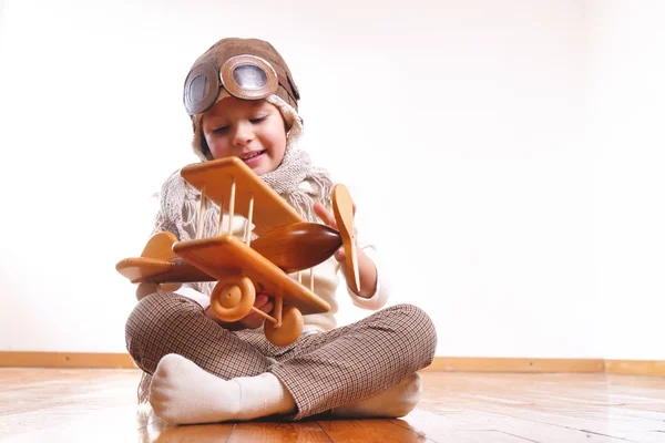 遊び心のある愛らしい少女に扮したパイロット木の床の上に座って 飛行機のおもちゃで遊んで — ストック写真